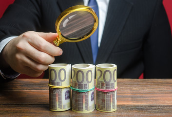 A businessman inspects a euro money bundle rolls through a magnifying glass. Search investments,...