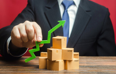 Businessman holding a green arrow up over boxes. Boost sales rate. Increasing production of goods,...