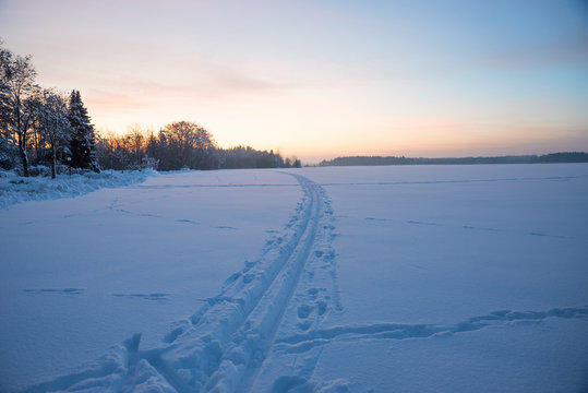 cross-country ski trail on snowy field, winter landscape at sunset