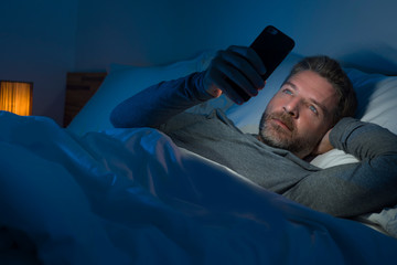 young attractive and relaxed man with blue eyes lying on bed late at night in dark and dim light...