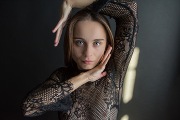 young pretty emotional and sexy girl with blue eyes in a black sweater holds her hands near her head and makes certain movements on her sun rays, low key