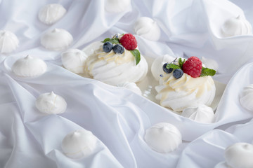 Dessert Pavlova with raspberries, blueberries and mint on a white fabric.