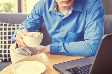 Businessman hold cup of coffee. A cup of coffee is on the table near the laptop.
