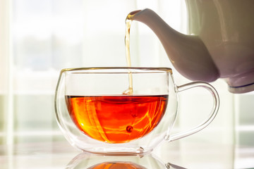 Fragrant strong tea pours from teapot spout in cup on table