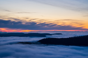 Fototapeta na wymiar Germany, Magical aerial view above endless fog clouds covering valley of swabian jura nature landscape at sunset with orange sky near stuttgart on mountain breitenstein