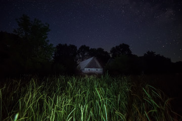 A small old house in the wilderness of the forest and the Milky Way with millions of stars above it. Night photo.