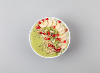 Healthy breakfast detox green smoothie with banana, kiwi, spinach, chia and pomegranate seed in a Bowl. Vegan food. Top view.