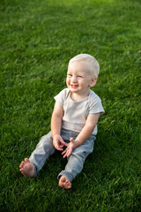 Little boy with blond hair laughs sitting on the green grass in the park