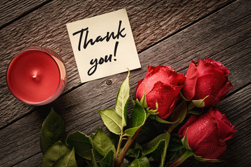Thank you note and red roses with aroma candles on a wooden background: concept of a romantic gift and thanks