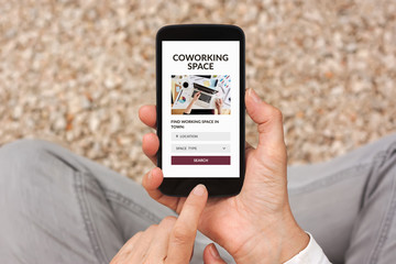 Hands holding smart phone with coworking space concept on screen. Top view
