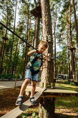 boy with safety carbine goes on a rope in adventure climbing high wire park