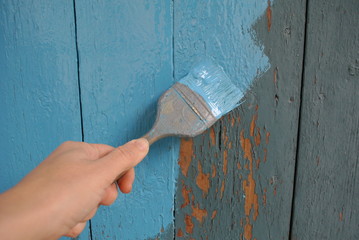 Painting a wooden fence with blue paint and paintbrush