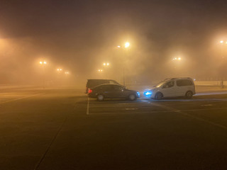 Kehl, Germany - Dec 04, 2019: Tight fog on the large parking illuminated by multiple lights and three parked cars