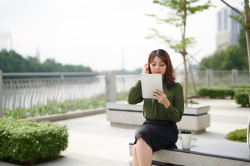 Beautiful woman sitting on bench using tablet outdoor.