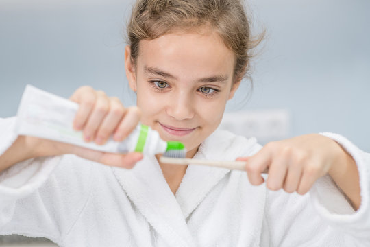 Smiling girl squeezing toothpaste on a toothbrush in the bathroom at home