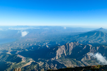 A view on volcanic island from the side of volcano Inierie in Bajawa, Flores, Indonesia. Few clouds below. Many volcanos in the back. Idyllic landscape. Endless horizon line.