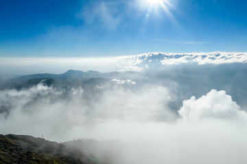 A view from volcano Inierie in Bajawa, Flores, Indonesia on a cloudy day. The slopes are barren with almost no plants. Big overcast below. Sun shining above the clouds. Nothing below is visible