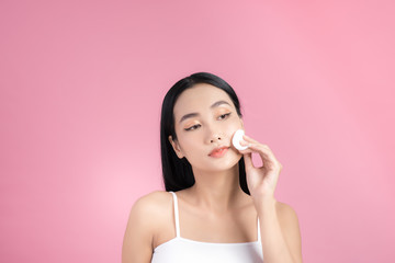 Crop attractive young female cleansing face with a cotton pad on a pink background in studio