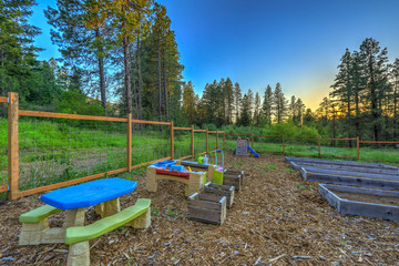 Large fenced in garden with kids play ground area and raised beds.