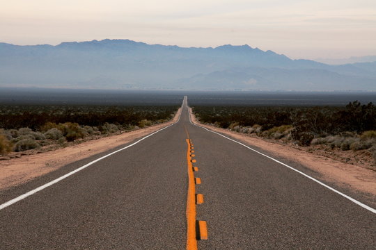 Long road towards the mountains in the California arid lands between Mojave Desert and Death Valley National park with the Sierra