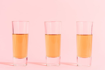 three shots with alcohol in row on pink background
