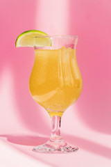 fresh yellow lemonade with lime slice in sunlight on pink background