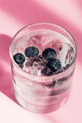Fototapeta na wymiar fresh lemonade with ice and blueberries in sunlight on pink background