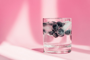 fresh lemonade with ice and blueberries in sunlight on pink background