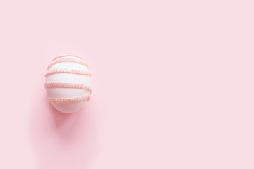 Easter egg decorated with mother of pearl sequin strip on a pastel pink background