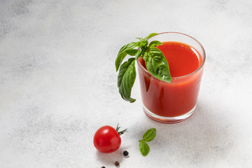Fresh tomato juice with basil in a glass on a light background.