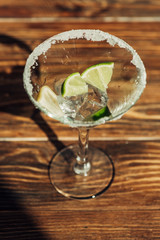 martini glass with ice, lemon and lime decorated with sugar on wooden surface in sunlight