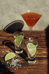 selective focus of fresh tequila with lime and salt and cocktail on wooden surface in sunlight