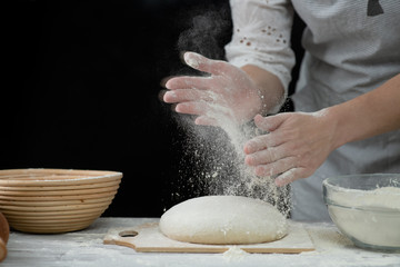 Chef sprinkl flour on a dough for cooking pastries, bread or pizza. Isolated on dark background