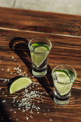 fresh tequila with lime and salt on wooden surface in sunlight