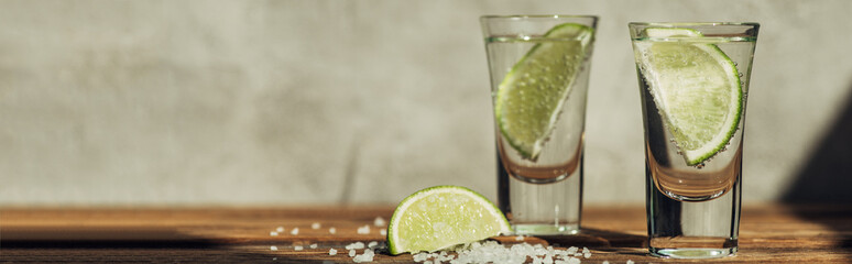 fresh tequila with lime and salt on wooden surface in sunlight, panoramic shot