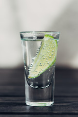 close up view of fresh tequila with lime on wooden surface
