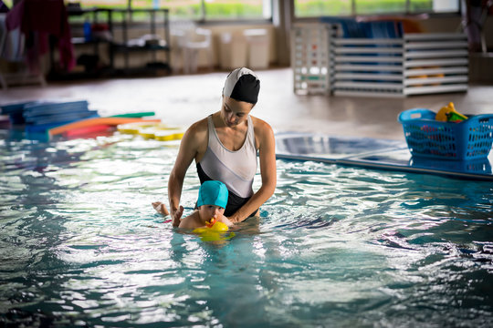 Girl in the middle of the indoor pool teaching a baby how to swim