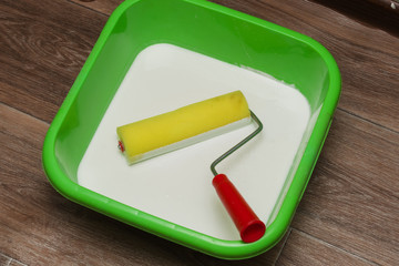 yellow roller with a red handle and a white primer in a green container, painting.