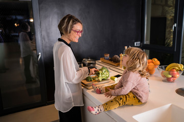 Mother cutting vegetables in the kitchen talking to a little girl sitting next to her