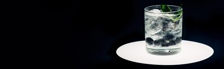 refreshing lemonade with ice and blueberries on illuminated circle isolated on black, panoramic shot