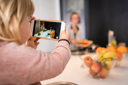 Little girl taking a picture with her mother's mobile while cooking