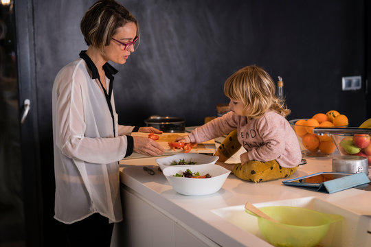 Mother preparing two salad plates in the kitchen talking to a little girl sitting next to her who helps her
