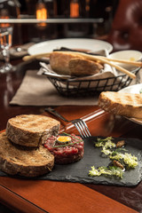 Steak Tartare with bread toasts served on stone plate on wooden table at restaurant