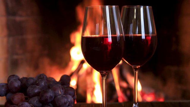 Two glasses of red wine with cheese and grapes near the fireplace