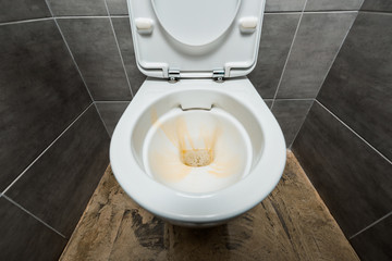 yellow liquid detergent in ceramic clean toilet bowl in modern restroom with grey tile