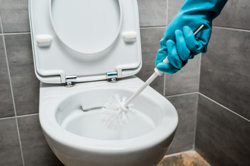 cropped view of cleaner cleaning ceramic toilet bowl with toilet brush in modern restroom with grey...