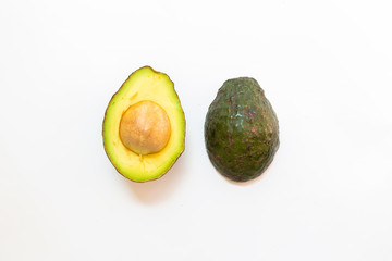 Avocado with green leaves on a white background. Green healthy fruit that is split in half and has a large seed inside.