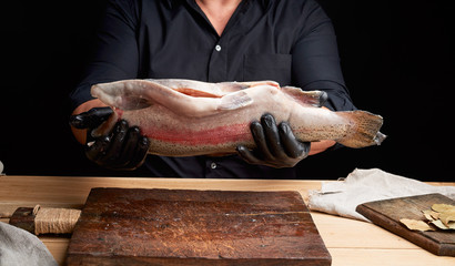chef in a black shirt and black latex gloves holds a raw carcass of headless salmon fish