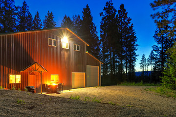 Large metal barn at night with fire at round table and outdoor furniture. © Iriana Shiyan