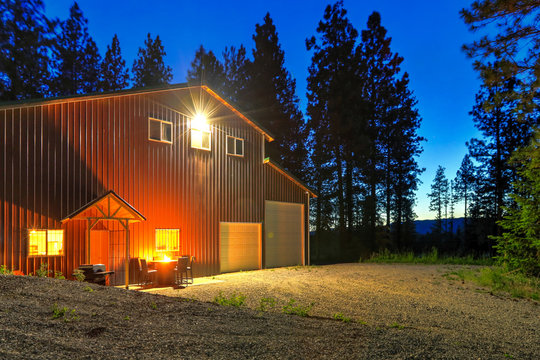Large metal barn at night with fire at round table and outdoor furniture.